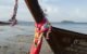the prow of a traditional long tail boat moored on the beach at phi phi island phuket. Wrapped around the prow are multi coloured ribbons and silks in tribute to buddha, known as the Buddha Point