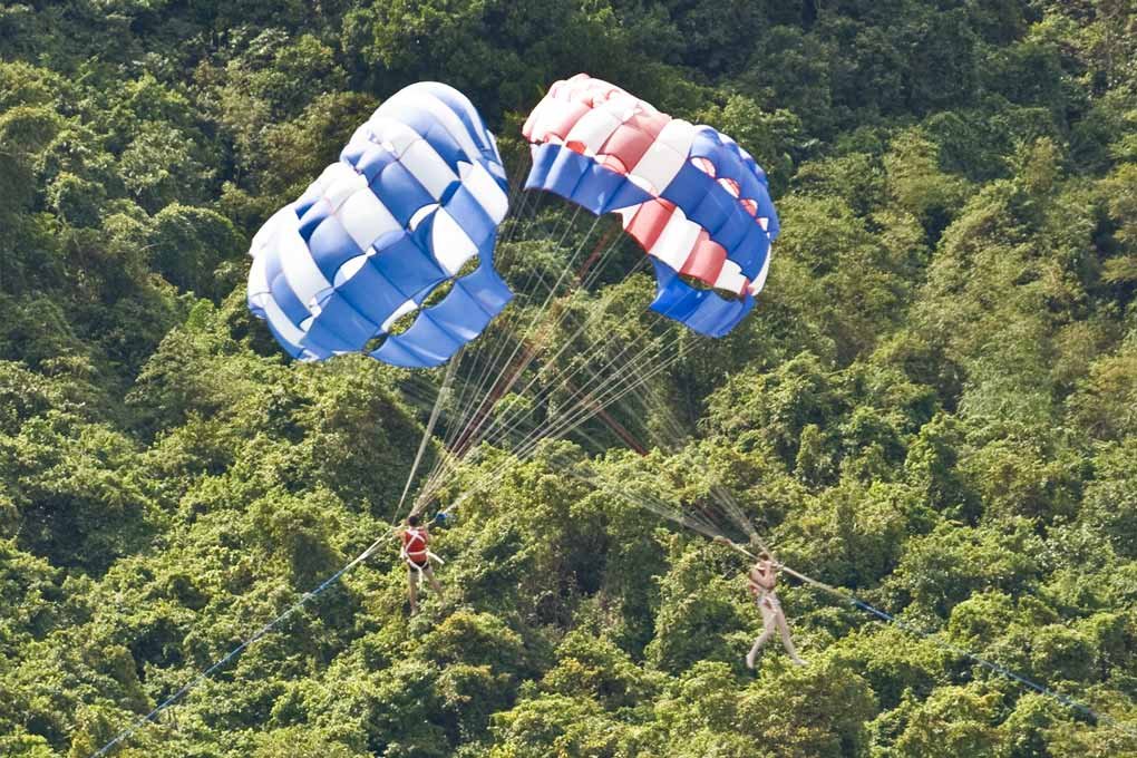 two holidaymakers crossing close by on their parasails against a jungle backdrop on the phuket coast